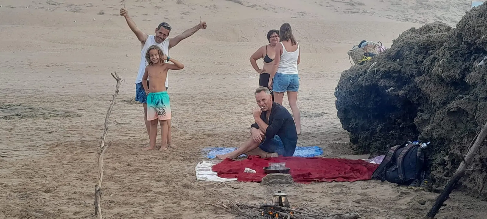 Une famille autour d’un petit feu et d’une théière, le soir, sur la plage