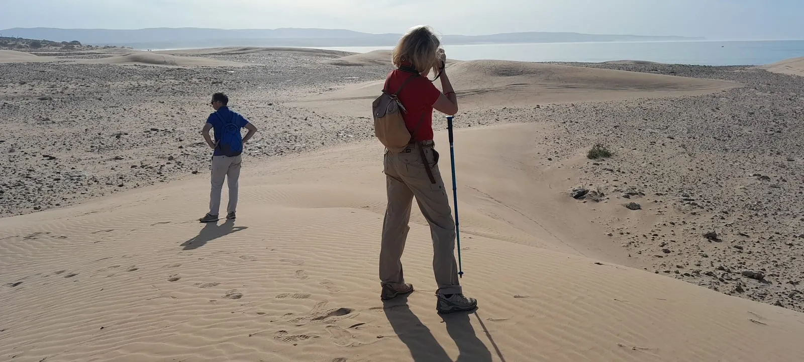 Une marcheuse photographie les dunes, de dos