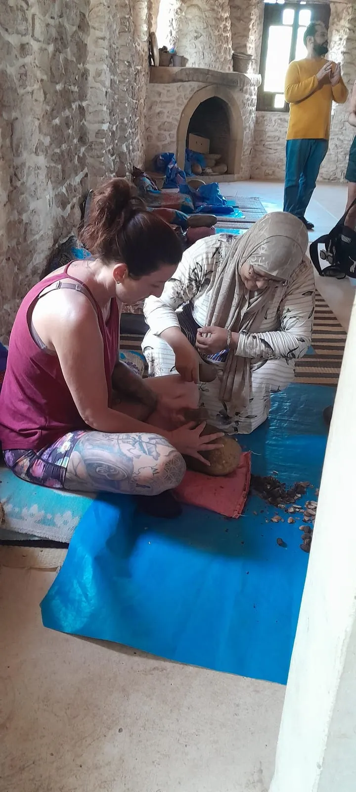 Une voyageuse concasse des noix d’argan aux côtés d’une femme du village