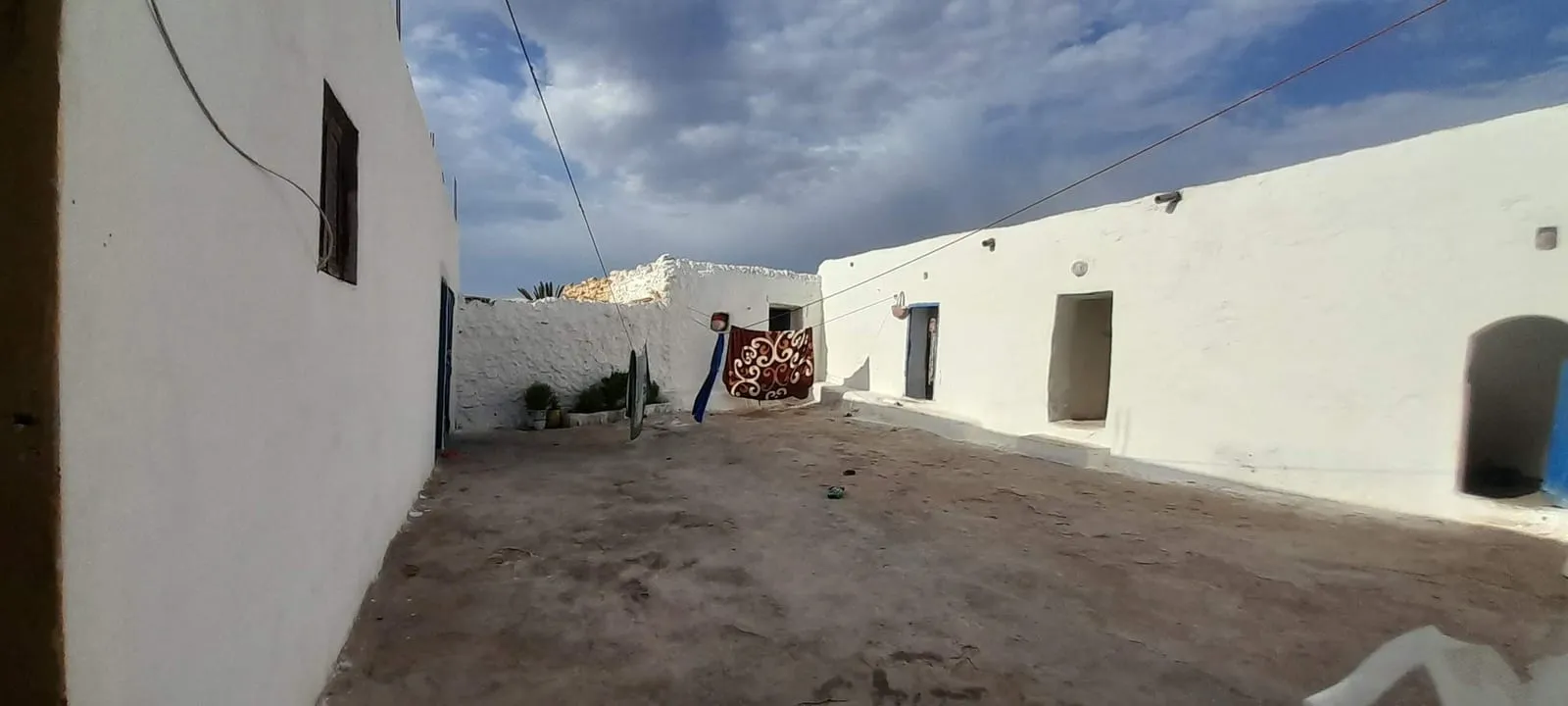 La cour blanchie de la maison, portes bleues et ciel chargé