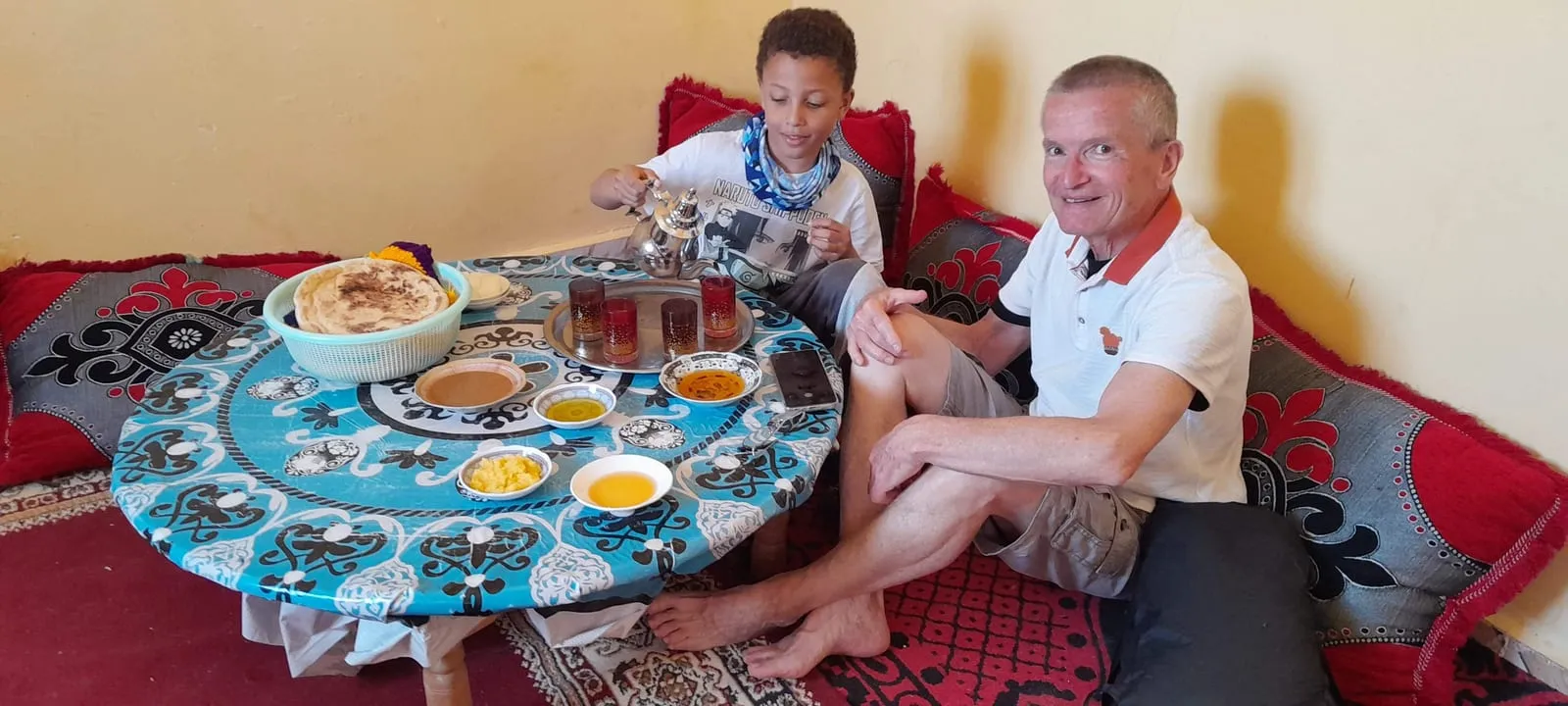 Un visiteur et un enfant attablés devant le thé, le pain et les bols d’huile et de miel