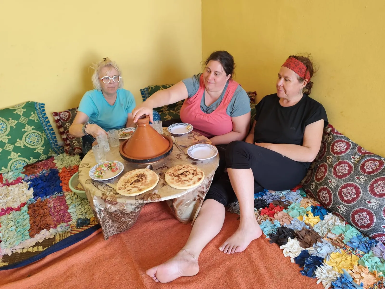 Trois voyageuses partagent un tajine et des msemen, assises sur les tapis