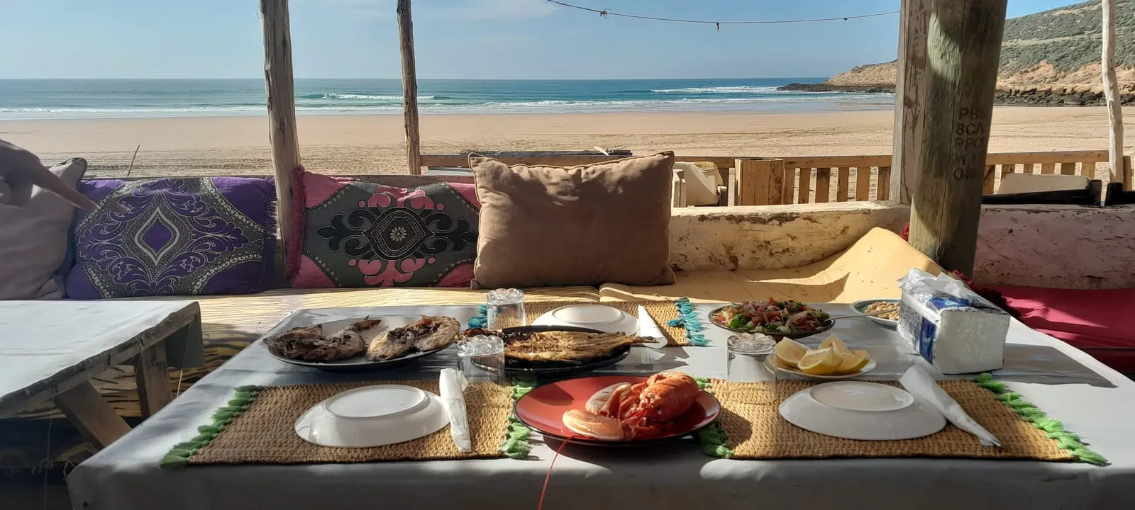 Table dressée face à la plage : poissons grillés, salades et pain