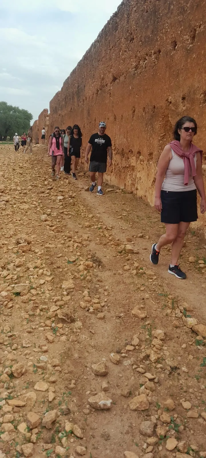 Le groupe marche sur le chemin caillouteux au pied des remparts de terre rouge