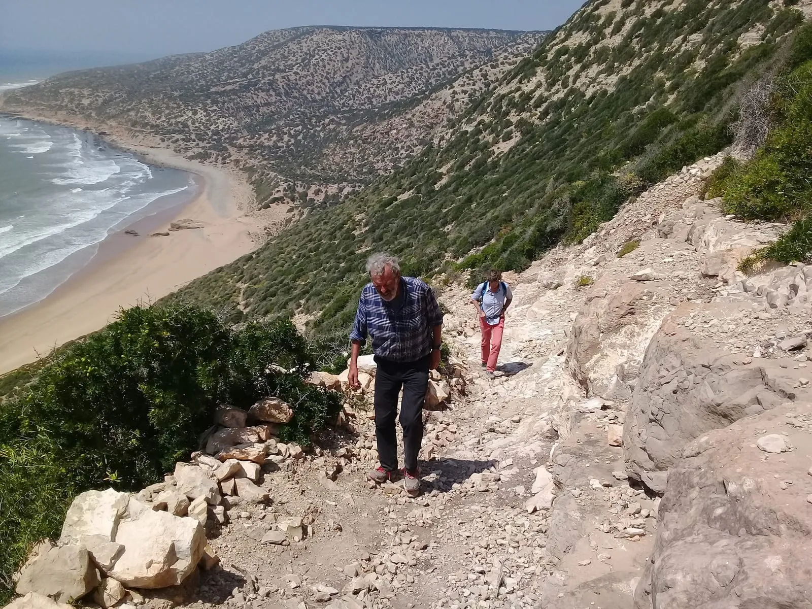 Deux marcheurs descendent le sentier pierreux au-dessus de la baie