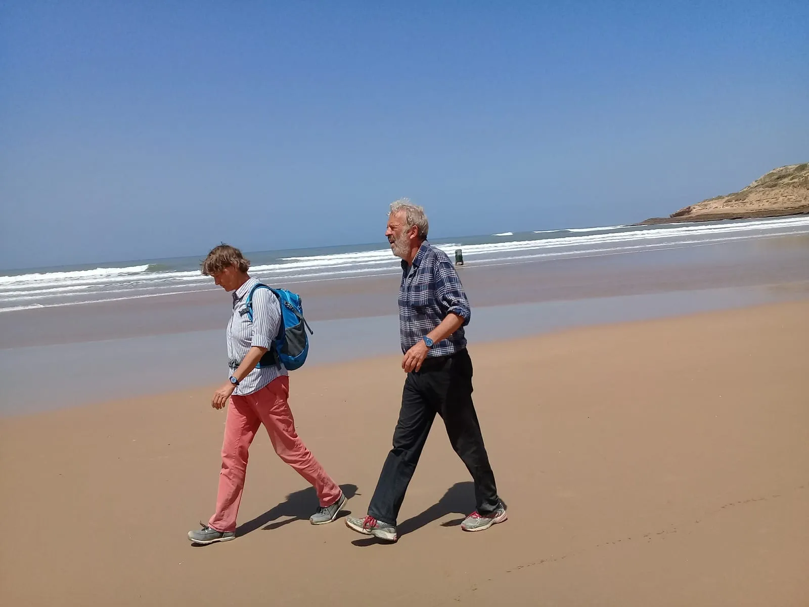 Deux marcheurs sur le sable mouillé, face au ressac