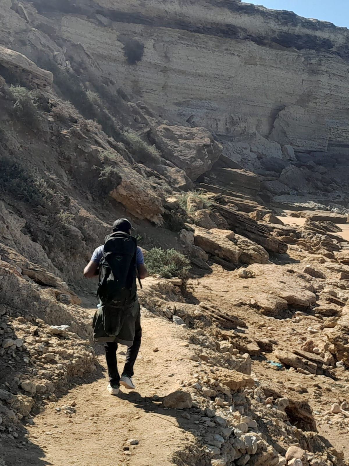 Kabir, sac au dos, sur le sentier au pied de la falaise, la plage au fond