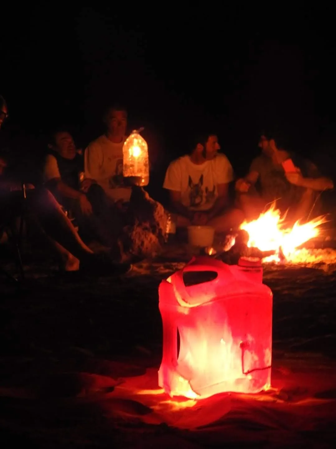Le groupe assis autour du feu la nuit, une lanterne accrochée au-dessus