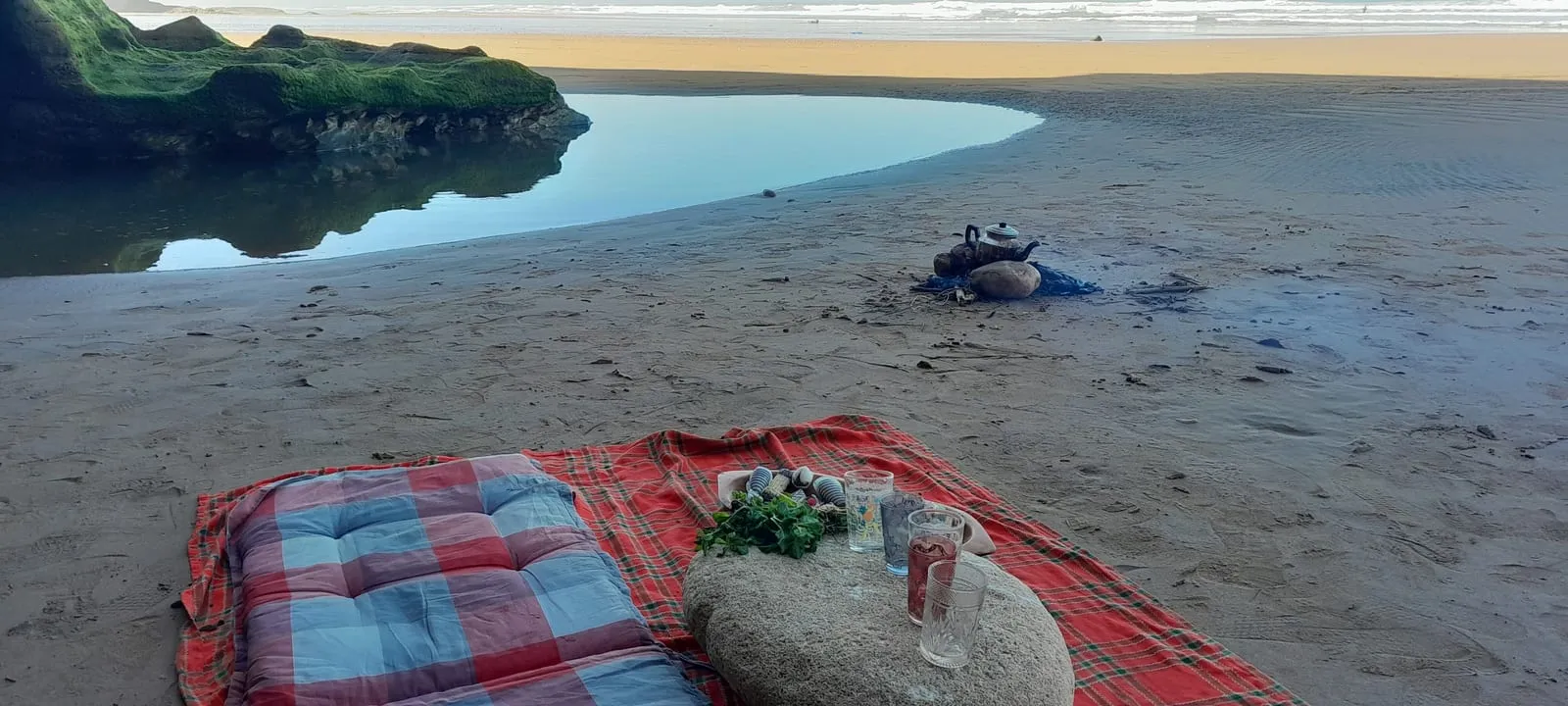 Matelas et couverture sur le sable, verres à thé et menthe posés sur une pierre