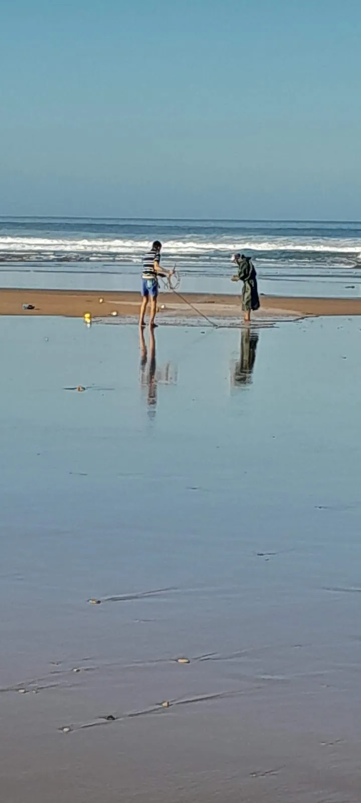Deux pêcheurs relèvent le filet sur le sable mouillé